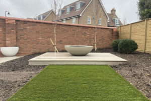 artificial grass walkway leading to decking and planter framed by two trees