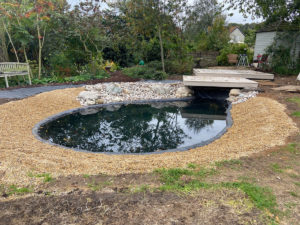 oval shaped wildlife pond with shingle banks and overhanging deck at one end