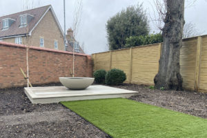 small square of composite decking with ivory coloured planter forming a water feature