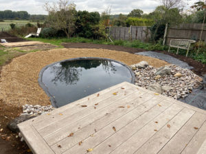 new pond and decking with trees reflected in the surface of the water