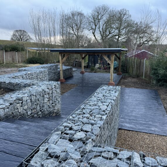 gabion retaining walls hugging composite decking steps and boardwalk leading to sturdy timber pergola